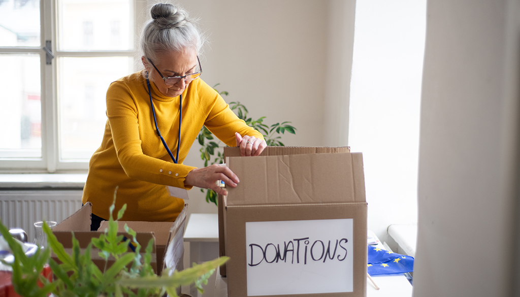 elderly woman packing box labeled donations
