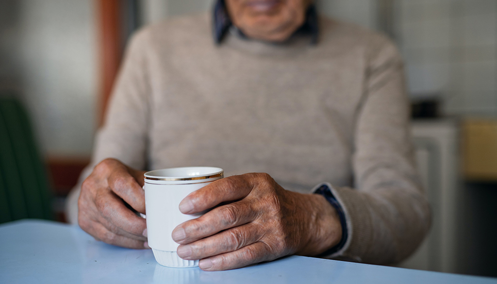 elderly man holding a coffee cup sitting at a table
