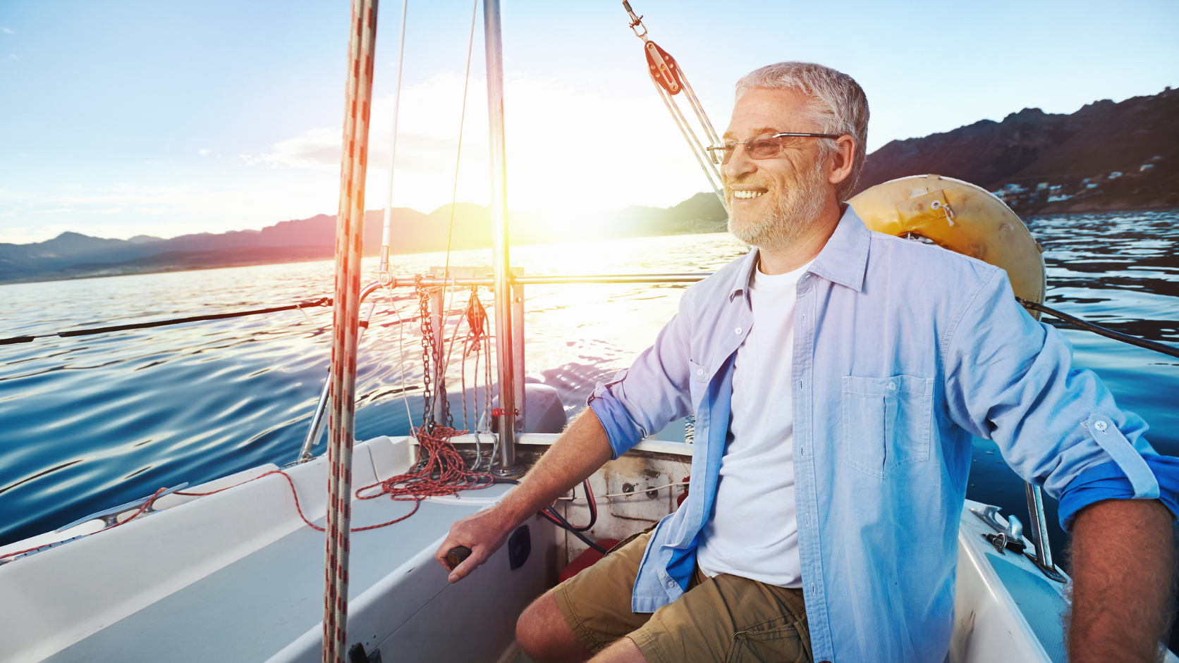 Older man sitting on a sailboat at sunset